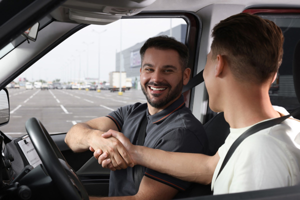 A learner driver adjusting the rearview mirror before starting a driving lesson, performing a cockpit drill.