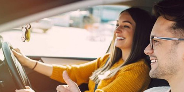 A driving instructor calmly gestures while providing guidance to a focused student driver from the passenger seat.