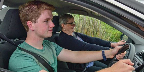 A young learner driver grips the steering wheel, listening intently to the driving instructor sitting beside them.