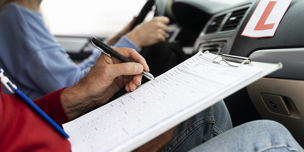 A close-up shot shows a student's hands confidently gripping the steering wheel, with the blurred road visible through the windshield.