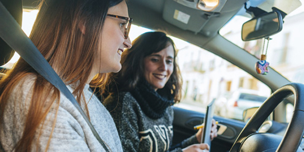 A smiling new driver proudly holds up their license while shaking hands with their cheerful and supportive driving instructor.